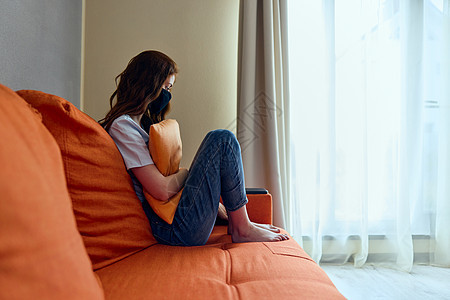坐在橙色沙发上 戴着保护面罩坐在家里的妇女不要离开家概念图片