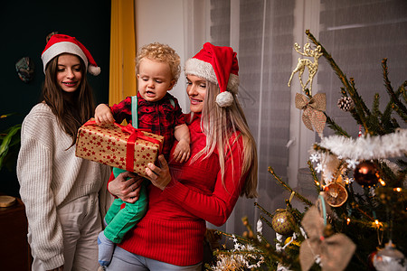 一个妈妈和大姐在圣诞节给一个两岁小孩送礼物幸福孩子圣诞女士儿子气氛传统居家季节彩灯图片