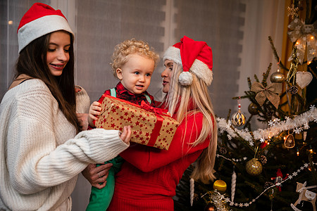 一个妈妈和大姐在圣诞节给一个两岁小孩送礼物儿子金发女郎教导传统气氛假期女士幸福女孩卷发图片