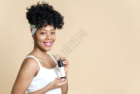完美清透粉底液一位美丽的黑人妇女在米色背景上拿着一瓶粉底液的画像 非洲裔美国年轻女性拿着一瓶粉底微笑背景