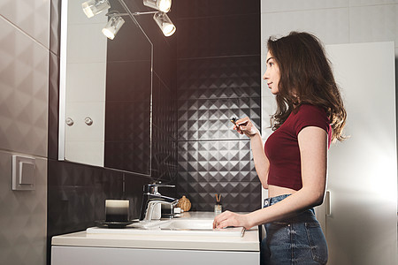女人在刷牙 年轻女人穿着勃根底顶部和牛仔裤 在镜子前拿着竹笔牙科竹子口服浪费牙膏牙刷女士浴室微笑生态图片