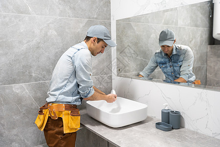 一个男人在浴室的柜子上 设置洗手盆龙头职业扳手修理工洗手间专家男性脸盆房子镜子图片