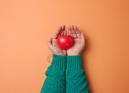 女性手握红心 橙色背景 爱与捐赠概念图片