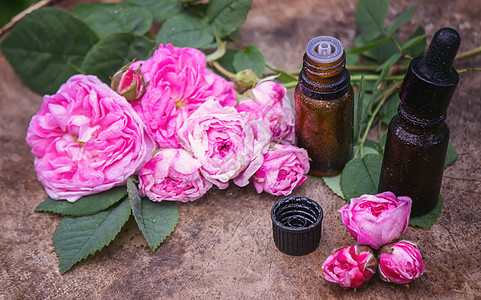 特写玫瑰基本油瓶 木制背景的叶子落下 笑声化妆品吸管植物温泉花瓣药品按摩香味芳香瓶子图片