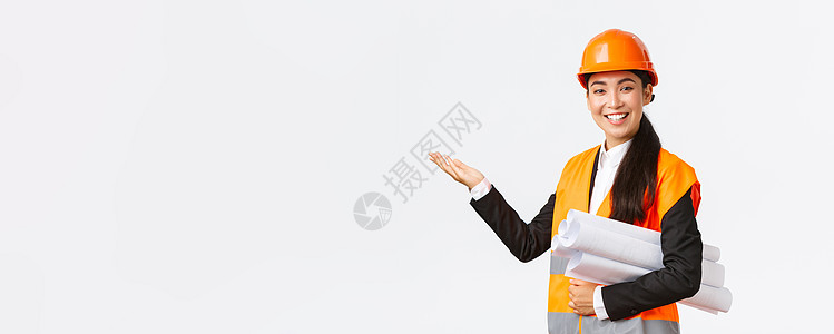 微笑的亚洲专业女建筑师 安全头盔工程师介绍建设项目 左手指着携带蓝图 发表演讲 介绍图表或建筑计划企业头盔幸福员工商业经理反光维图片