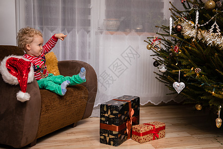 一个笑着的两岁小孩 将手指指向圣诞树传统庆典肤色树灯积分椅子栽培卷发客厅氛围图片