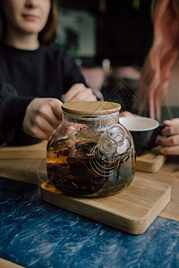 女孩把茶壶里的茶倒到白色杯子上 美丽的女人带着绿色的毛衣笑容 她很可爱成人咖啡饮料冲浪厨房键盘女士女性微笑食物图片