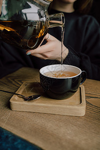 女孩把茶壶里的茶倒到白色杯子上 美丽的女人带着绿色的毛衣笑容 她很可爱饮料女性食物女士冲浪键盘休息厨房咖啡店微笑图片