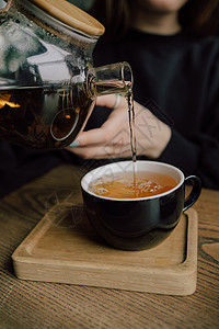 女孩把茶壶里的茶倒到白色杯子上 美丽的女人带着绿色的毛衣笑容 她很可爱女性女士桌子厨房微笑咖啡休息饮料食物键盘图片