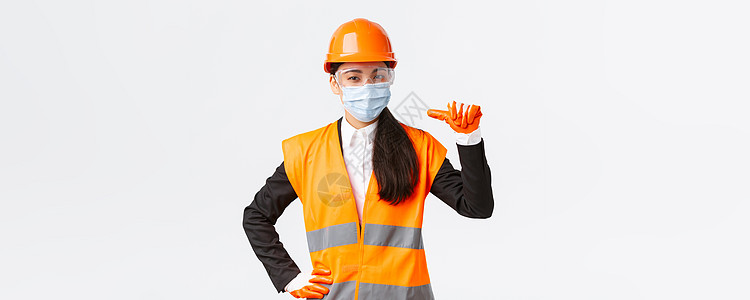 Covid19 在企业 建设和预防病毒概念方面的安全协议 自信的亚洲女工程师戴着头盔和面罩指着自己 宣传个人协助女孩商业快乐建筑图片