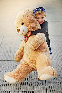 熊越大 拥抱越大 一个可爱的小女孩在外面玩耍时抱着一只巨大的泰迪熊的画像图片