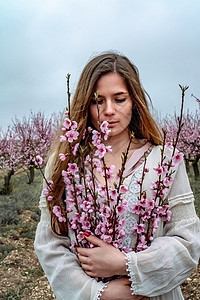 穿蓝裙子 长头发的年轻美女 正在享受着盛开花蜜桃树植物女孩柳条花园香气黑发太阳露天微笑公园图片