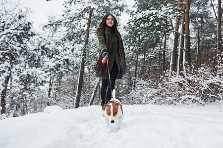 穿着暖身衣的女人在雪林里走着狗的行走图片