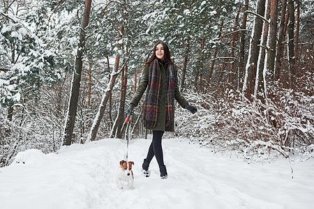 穿着暖身衣的女人在雪林里走着狗走 前视线图片