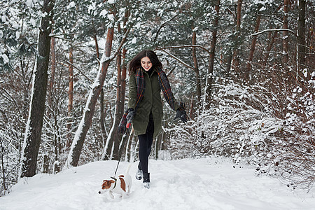 穿着温暖衣服的女人在雪林里走着狗 前视线图片
