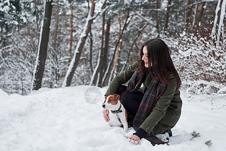 与她的狗一起在冬季公园散步时欢乐地笑着的褐发黑发女郎图片