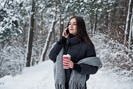 在电话上聊天 穿暖身衣的女孩喝咖啡 在冬季森林散步吧! (Y 我)图片