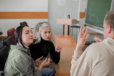 两个女孩和一个男人正在用手语交谈 三名聋哑学生在大学教室里聊天男生班级手臂快乐讲话男人朋友们手指耳朵手势图片