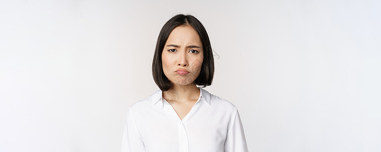 悲伤而阴郁的亚洲年轻女性做鬼脸 皱眉 心烦意乱 噘着脸 白色背景冒充工作室快乐管理人员企业家手臂人士标识女士办公室图片