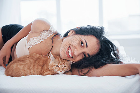 迷人的金发美女和可爱的小猫睡在白床边上衣服宠物奢华头发女士枕头微笑女性时间情感图片