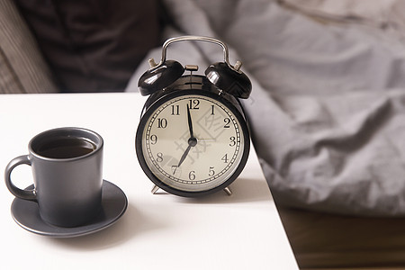 一张黑色咖啡杯的图像闹钟在床前白床边桌子上 上面有灰色麻布 房间在米色调中寝具活力卧室咖啡唤醒乐趣早餐杯子床头女性背景图片