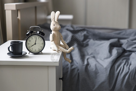 一张黑色咖啡杯的图像闹钟在床前白床边桌子上 上面有灰色麻布 房间在米色调中时间咖啡兔子早餐野兔活力手表卧室玩具苏醒背景图片