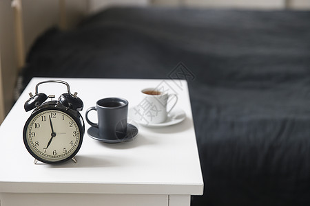 一张黑色咖啡杯的图像闹钟在床前白床边桌子上 上面有灰色麻布 房间在米色调中床头卧室杯子早餐苏醒时间寝具女性咖啡乐趣图片