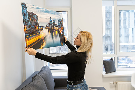 女人把摄影挂在白墙上 手拿着照片画布印着纸 笑声女性房间女孩技术旅行画廊打印风格艺术装潢图片