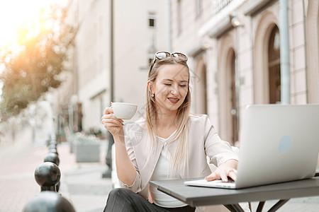 女自由职业者坐在户外咖啡厅的桌子上工作手机博客商业城市咖啡店餐厅博主微笑咖啡技术图片