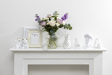 白色咖啡桌上放着玻璃花瓶中的 紫色和白色玫瑰 小茶玫瑰 和蓝色鸢尾花束 灰墙图片