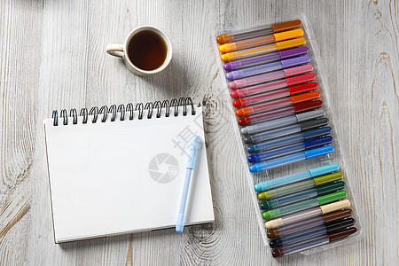 从上面查看 24个彩色标记和笔记本都在绘图桌上蓝色画板杯子毛毡药片毡笔墨水记事本教育桌子图片