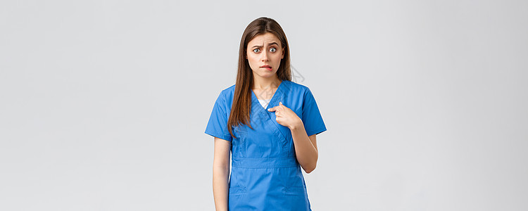 医护人员 预防病毒 保险和医学概念 紧张而困惑的女护士 穿着蓝色磨砂膏的医生 咬着嘴唇焦虑地指着自己 困惑地等待着答案外科医师科图片