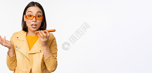快乐的亚洲女孩用免提电话交谈 录音 用手机应用翻译她的声音 用智能手机动态交谈 站在白色背景上的形象学生情绪太阳镜互联网工作技术图片