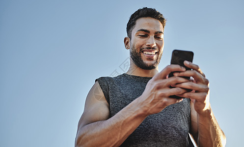 在现代科技的帮助下建立肌肉 一个运动青年在户外锻炼时使用手机的低角度拍摄手势 校对 Portnoy图片