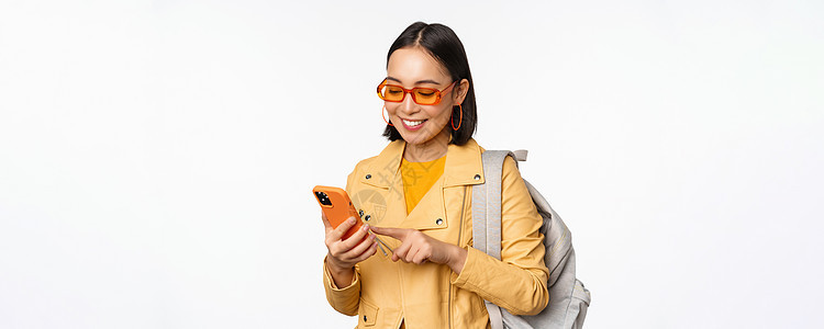 时尚的年轻女性女游客 带背背包和智能手机旅行者在镜头下微笑 以白色背景装扮情感互联网女士商业技术大学工作办公室促销广告图片