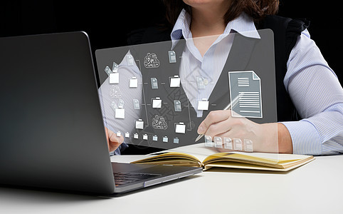 女人坐在桌子旁 用笔记本电脑工作 文档管理系统 (DMS) 用于自动化归档和高效管理的软件图片