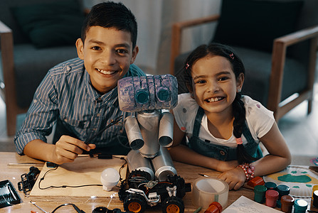 有两个可爱的年轻兄弟姐妹的肖像 和他们新造的玩具机器人一起装扮在家中 这简直是一团糟图片