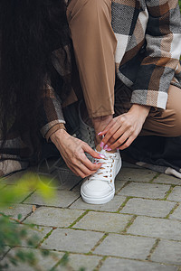 身穿长大衣和米裤的年轻女子的照片 女士在市街上摆姿势 妇女在运动鞋上贴着丝带城市魅力裤子女孩街道达人头发鞋带冒充成人图片