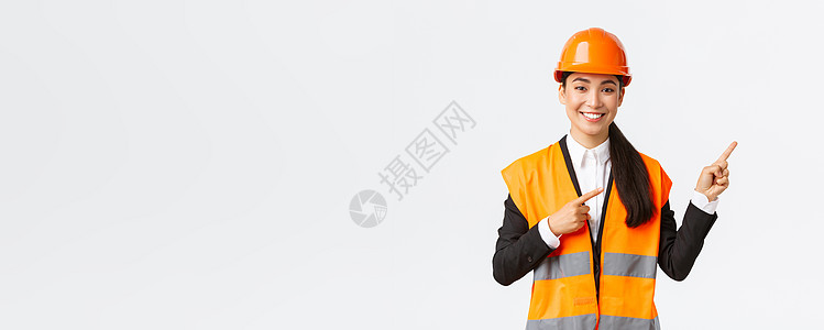 建筑 施工和工业概念 身着安全头盔和反光服的微笑亚洲女工程师展示物品 右指 女售货员向客户介绍房产领导者经纪人办公室电子商务经理图片