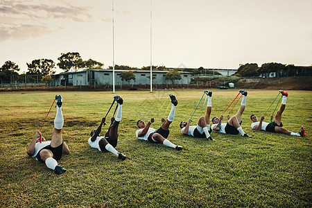 阻力训练将您推出舒适区 白天 一群年轻的橄榄球运动员在球场上与乐队一起训练的全长镜头图片