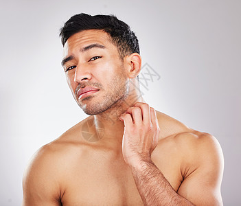 一位年轻男子的肖像检查他的皮肤 在做皮肤护理时不高兴 他穿着灰色背景的皮革照样图片