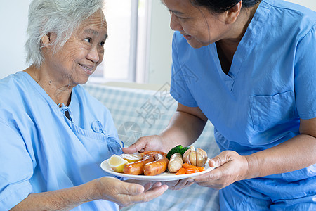 亚洲年长或年长的老妇人病人坐在医院的床上饿着肚子吃早餐和蔬菜健康食品 充满希望和快乐办公室护士外科药品房间女士说谎男性退休手术图片