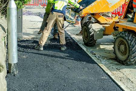 建筑工人在道路工程和人行道修补期间放置热薄凝油布图片