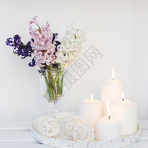 米色的桌子上放着一束白色 粉色 蓝色的切花风信子 放在一个白色的小波纹花瓶里 圆盘上放着三支燃烧的大蜡烛 放置文本图片