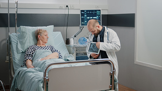 医生指着用放射线为患病妇女显示平板电脑的陈列器药物x射线长老男人房间专家保健诊所药品外科图片