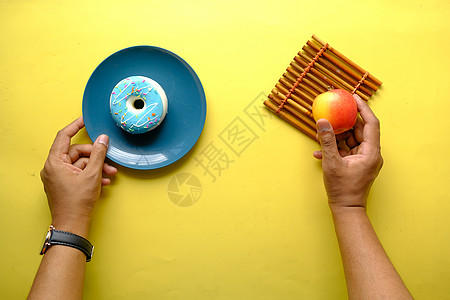 蓝色背景的手持甜甜圈和苹果保健重量垃圾测量卫生营养背景图片