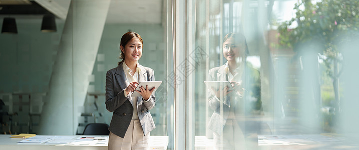 站在窗户旁边 使用智能数字平板电脑的有吸引力的女商务人士工作职场职业商务女士成人商业员工笔记本成功图片