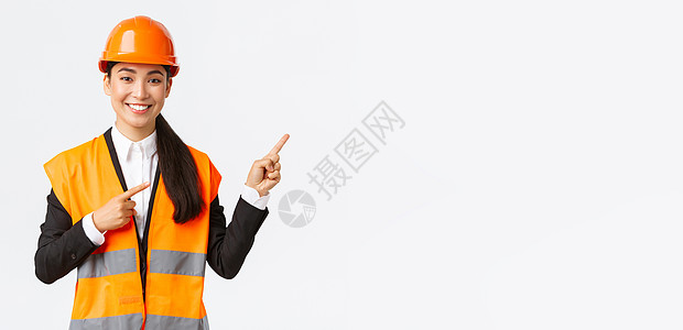 建筑 施工和工业概念 身着安全头盔和反光服的微笑亚洲女工程师展示物品 右指 女售货员向客户介绍房产领导者经理头盔电子商务夹克雇主图片