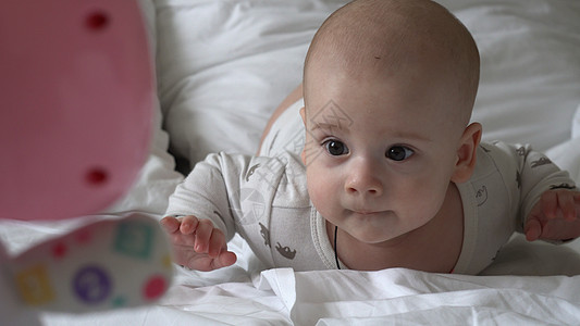 特写快乐顽皮的孩子 6 个月大 刚出生的男孩在白色柔软的床上沐浴后看着相机 宝宝睡前用玩具醒来的时间 童年 母亲 家庭 婴儿概念图片
