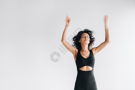 一个穿黑色运动服的女子 在白色背景下跳起来 举起双臂高举起来的模糊轮廓运动员工作室女性状况幸福快乐女孩喜悦女士冥想图片
